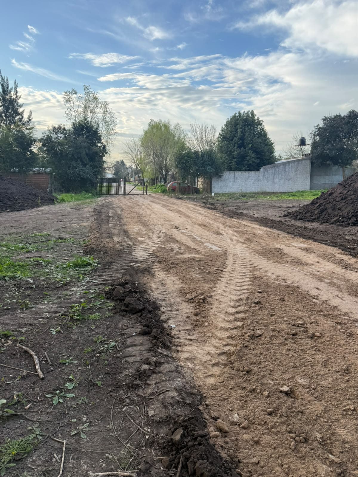 Calle abierta con movimiento de suelos hacia el portón de acceso del predio